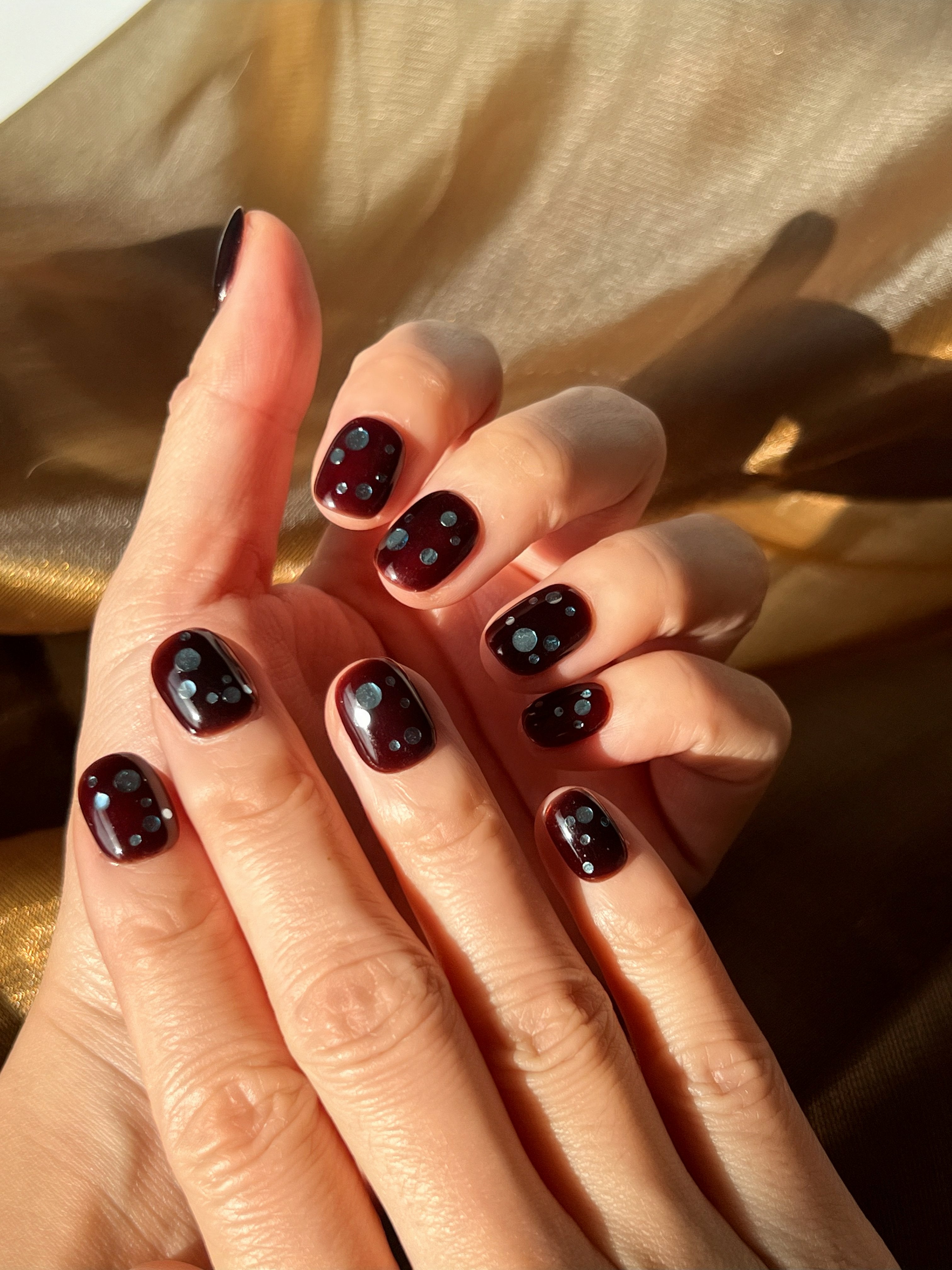 Espresso brown press-on nails with soft blueberry-toned dots, worn on hand in warm winter light