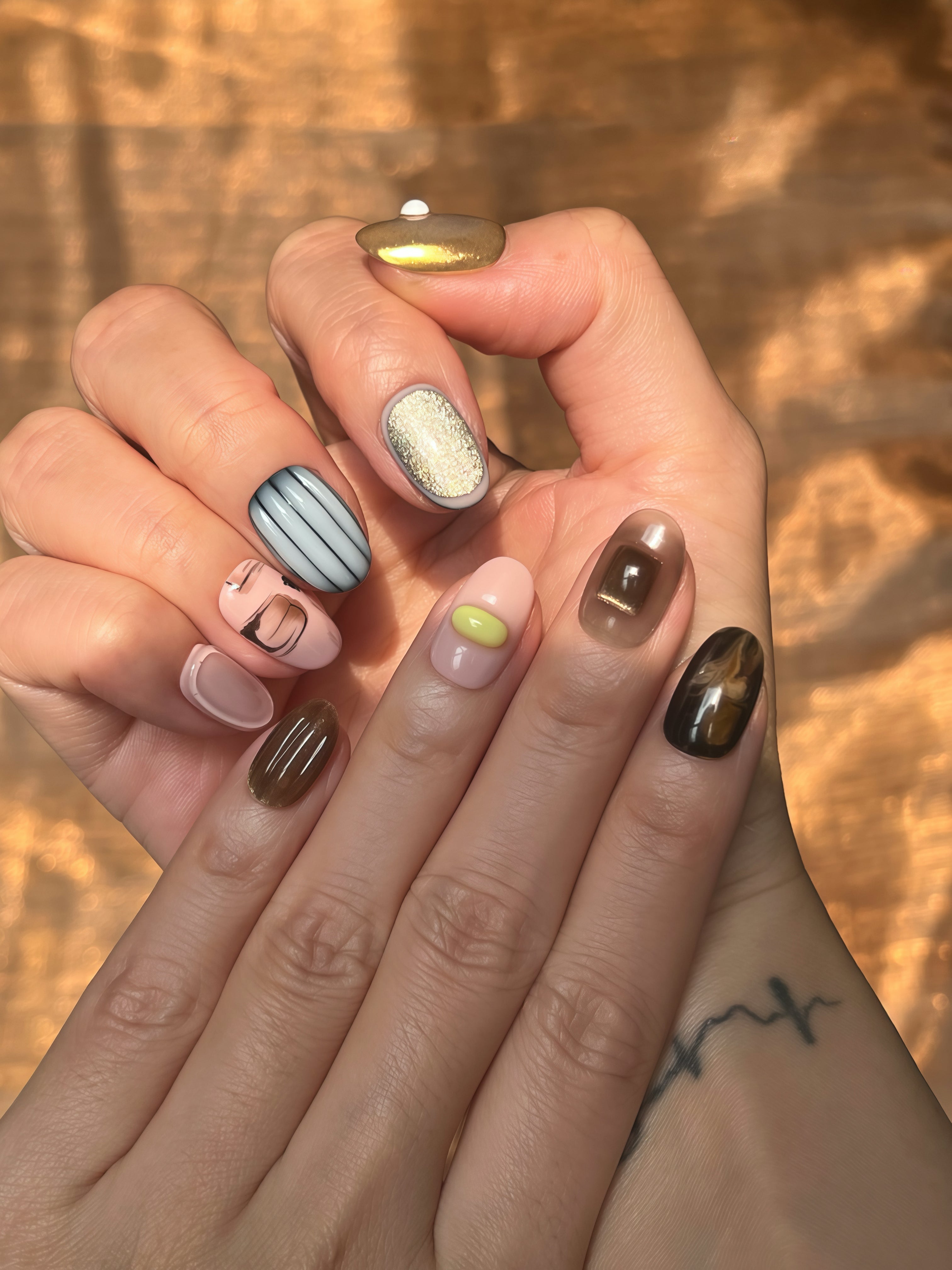 Hand wearing Flowing Dawn autumn-inspired press-on nails with warm brown and gold accents — designer reusable nail set.