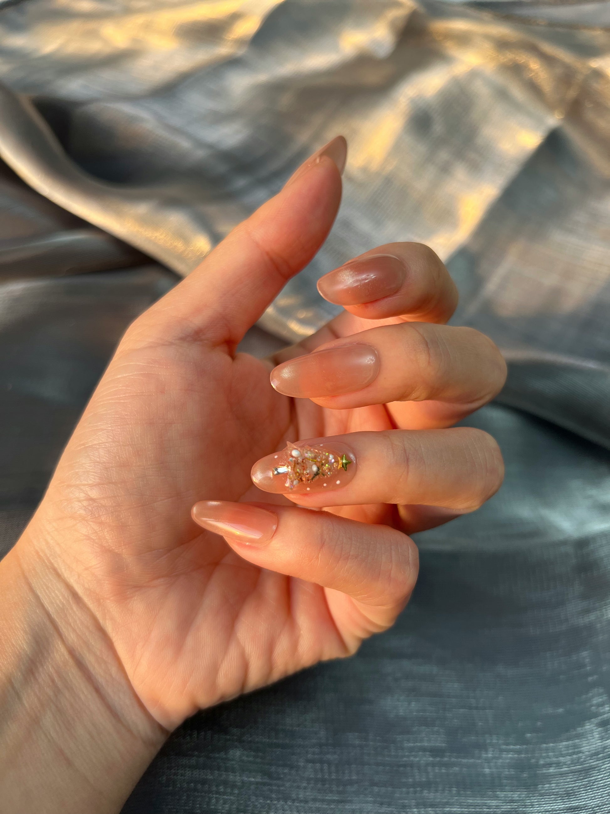Golden Fir nude-gold press-on nails with a handcrafted 3D Christmas tree made from gems and micro-pearls, shown in a close-up hand shot under warm winter light.