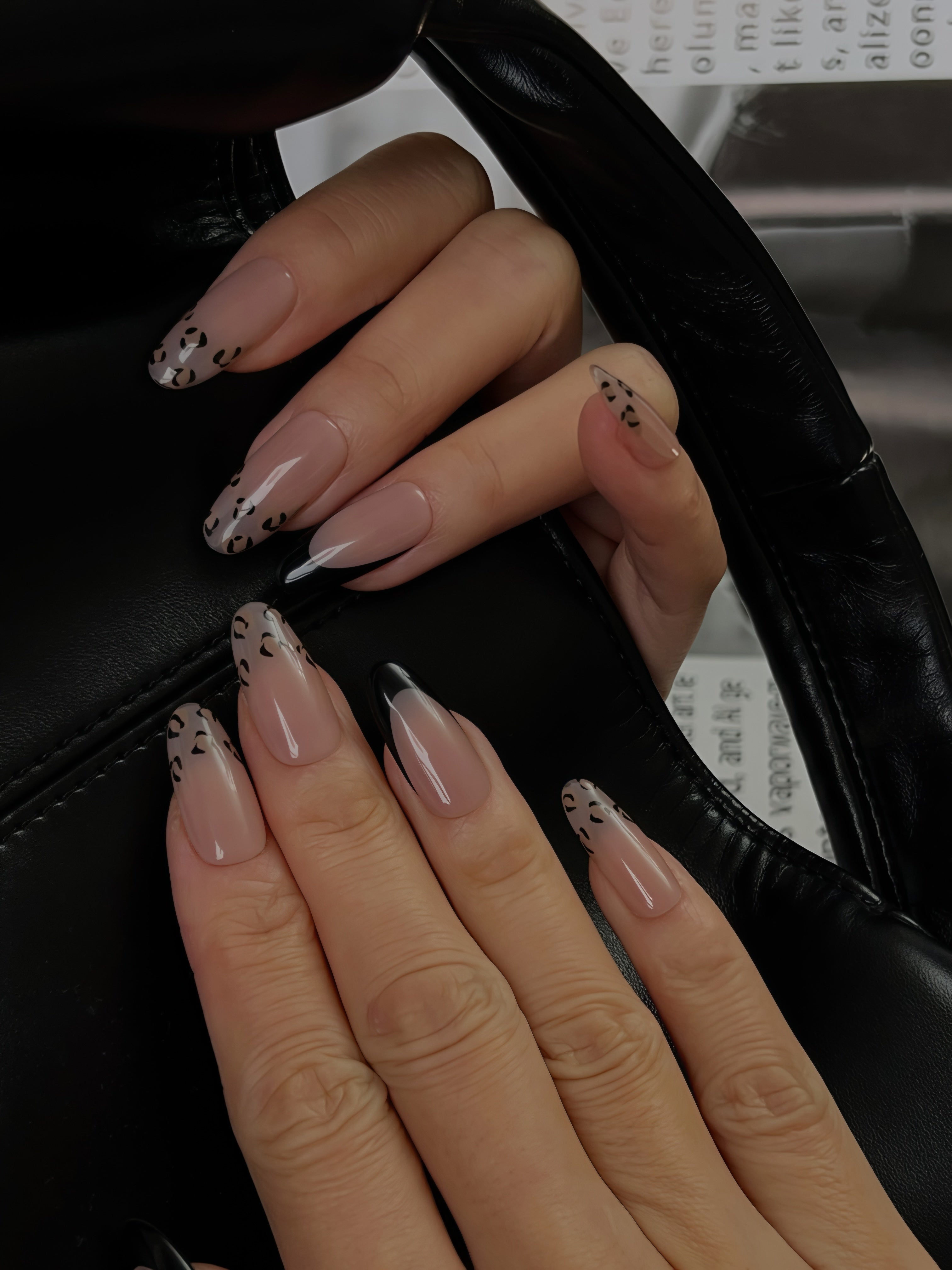 Nude French press-on nails with black leopard tips, worn on hand holding a black leather bag — Midnight Temptation by Momento.