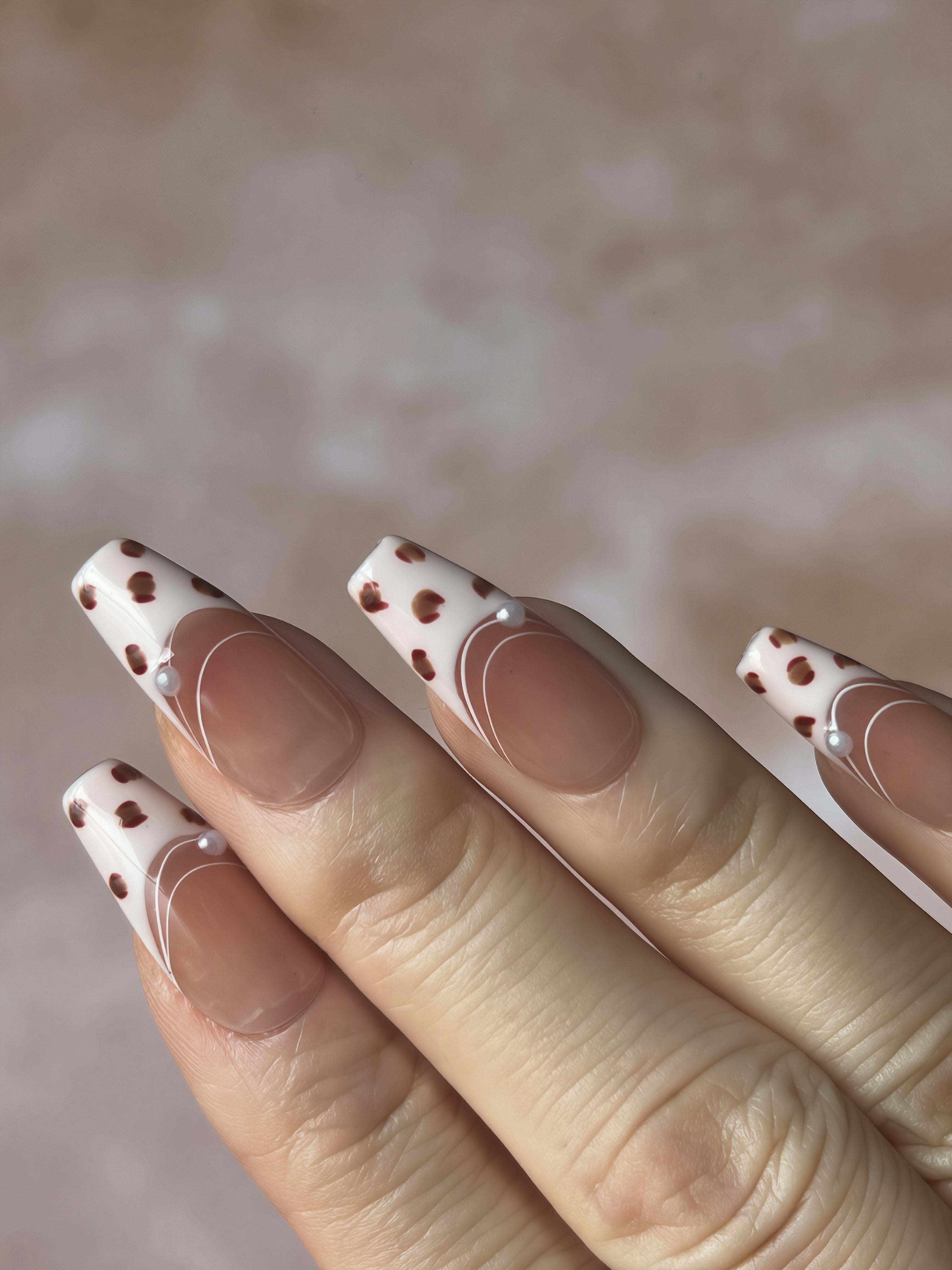 Hand pose showing Gentle Wild press-on nails with blush-pink French tips, playful leopard spots, and subtle pearl details.